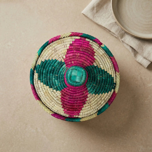 Overhead top-down view of a circular Mazari palm basket lid featuring a symmetrical teal and fuchsia geometric woven pattern.