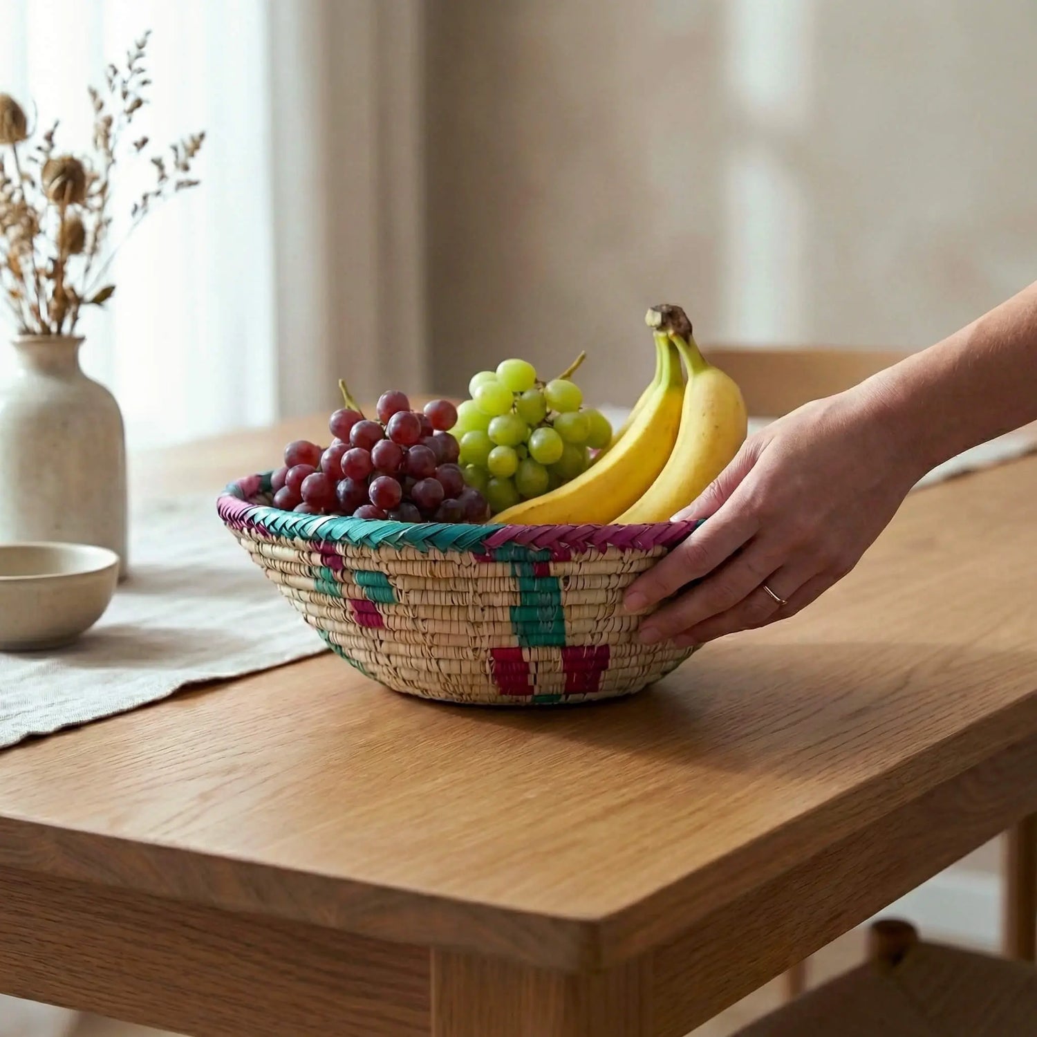 The SHKOR Mazari basket used as a natural fruit bowl on a wooden dining table.